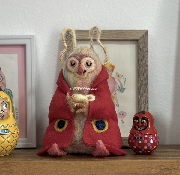 Figura en fieltro de una polilla con capa roja y ojos grandes